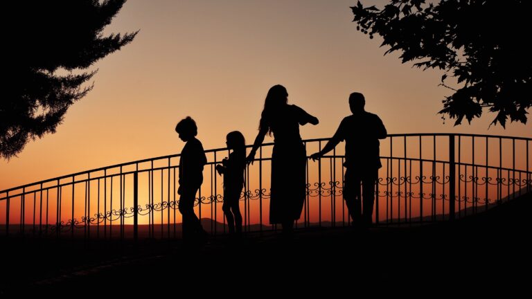A family enjoying a beautiful sunset silhouetted on a bridge, creating a heartwarming scene.